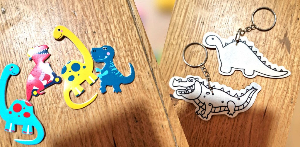 A collection of colourful dinosaur-shaped magnets in various designs, alongside two dinosaur keychains featuring a cartoonish dinosaur and a crocodile.